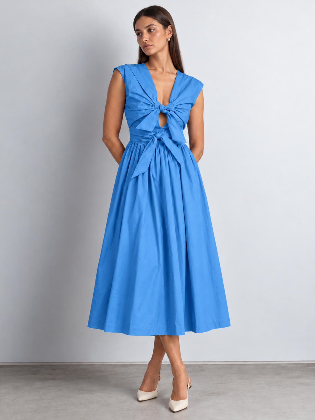 a women wearing blue midi dress with adjustable bows detailing at the front bodice posing against a white backdrop