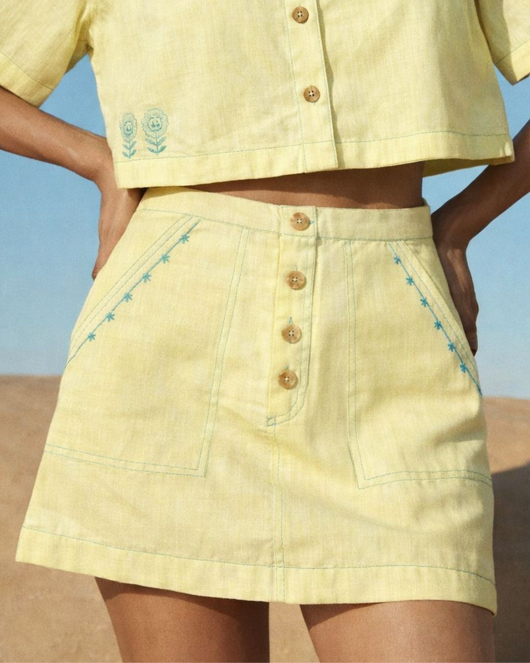 Person wearing a yellow outfit with buttons and embroidery against a clear blue sky.