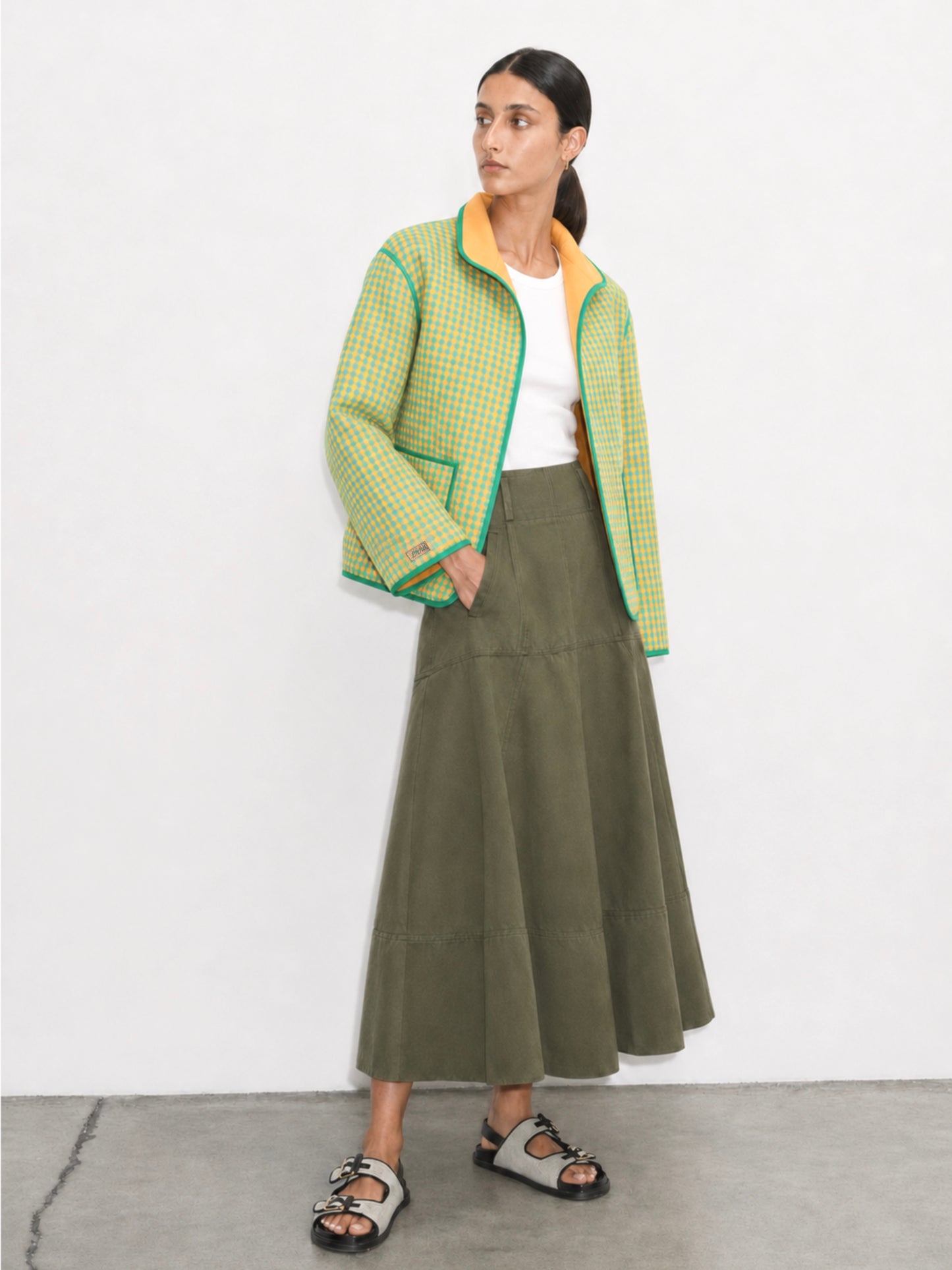 Woman wearing a green checkered jacket and olive green skirt on a white background