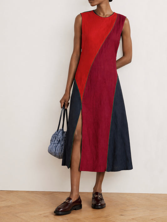 Woman wearing an upcycled, multicoloured dress holding a blue bag against a white background 