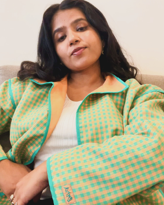 Woman wearing a green and yellow checkered reversible jacket sitting on a couch.