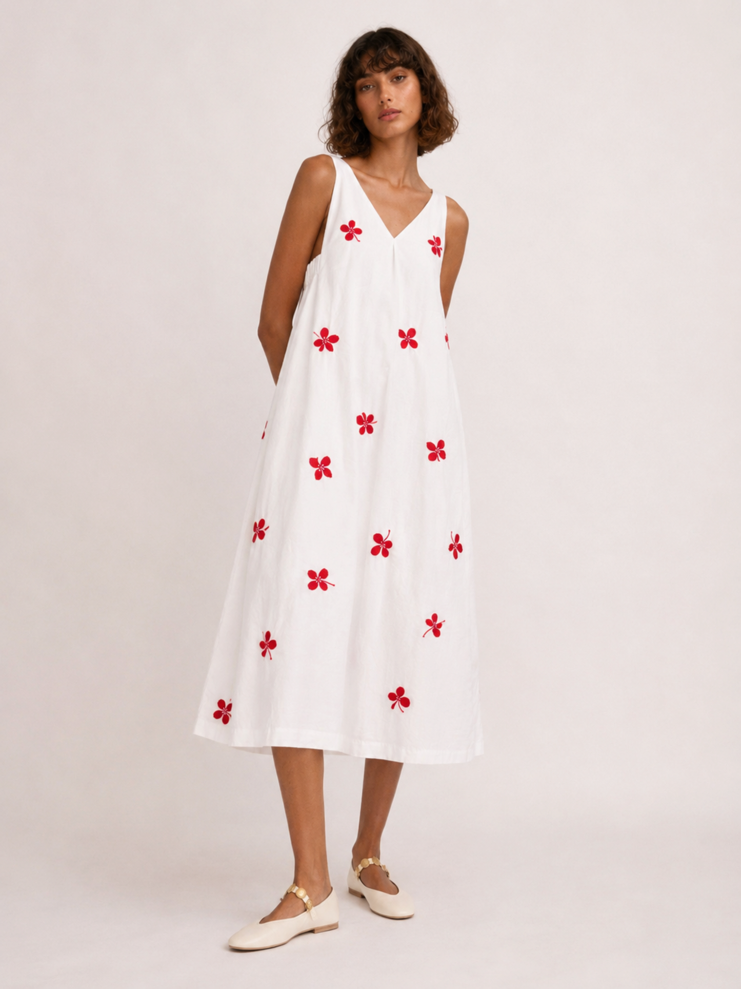 Woman wearing a white dress with red floral patterns on a plain background
