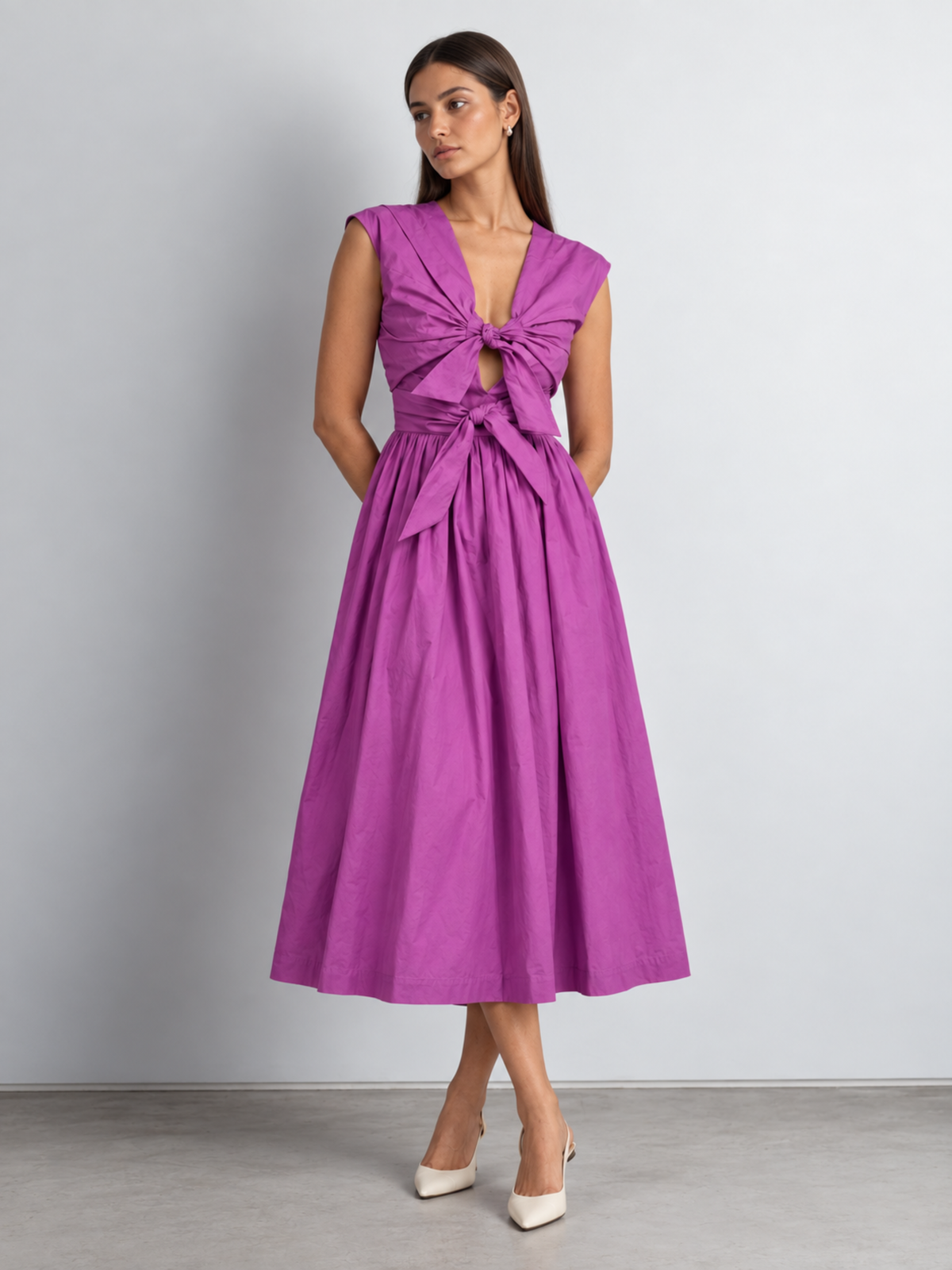 a women wearing purple midi dress with adjustable bows detailing at the front bodice posing against a white backdrop